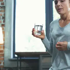 Kobieta z objawami uderzeń gorąca, szukająca naturalnych sposobów na menopauzę, pije wodę.
