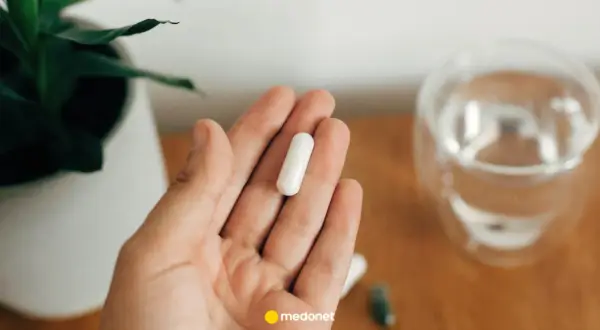 Dłoń trzyma białą kapsułkę. Obok szklanka wody. Uważaj na nadmiar magnezu objawy, by nie przedawkować.